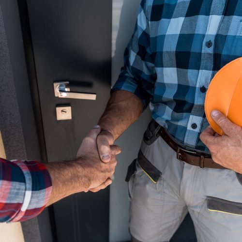 cropped view of builders shaking hands while standing near door