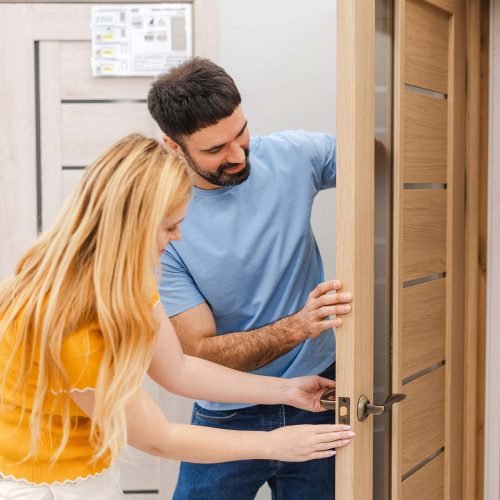 Portrait of happy married young couple choosing interior door at store market while touching, checking the quality
